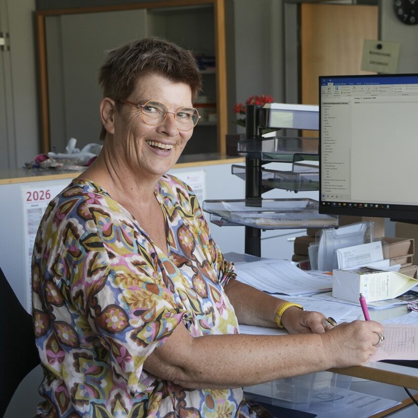 Foto Sekretariat Rauscher Frau Rauscher vom Sekretariat sitzt lächelnd an ihrem Schreibtisch.