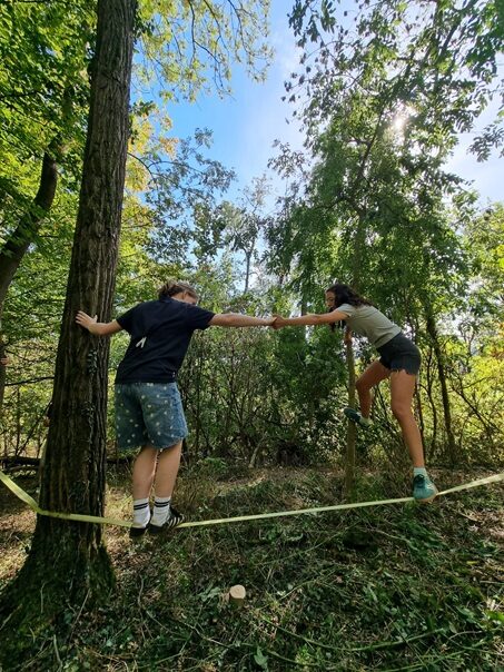 Schüler der Klassenstuufe 9 helfen sich gegenseitig, eine Seilbrücke im Wald zu überqueren.