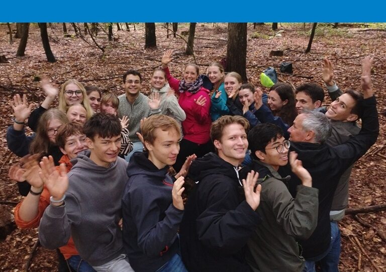 Schüler*innen des Bio LK machen im Wald ein gruppendynamisches Spiel, bei dem sie sich gegenseitig auf den Schenkeln sitzen, ohne, dass der Kreis umfällt.