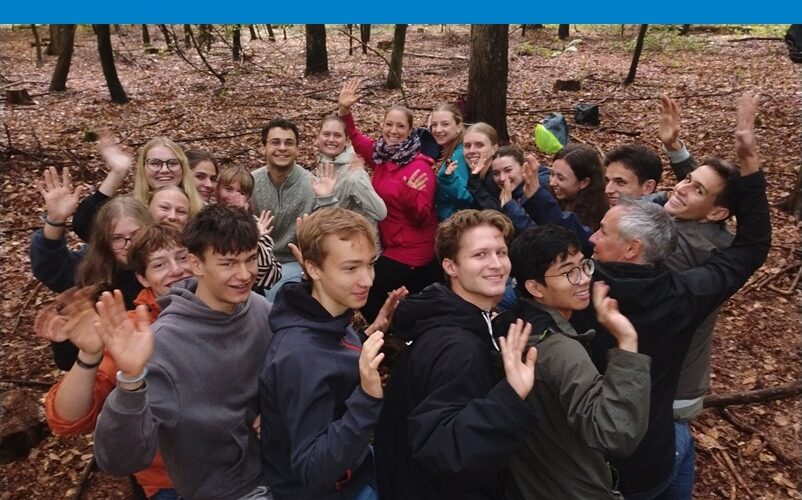 Schüler*innen des Bio LK machen im Wald ein gruppendynamisches Spiel, bei dem sie sich gegenseitig auf den Schenkeln sitzen, ohne, dass der Kreis umfällt.